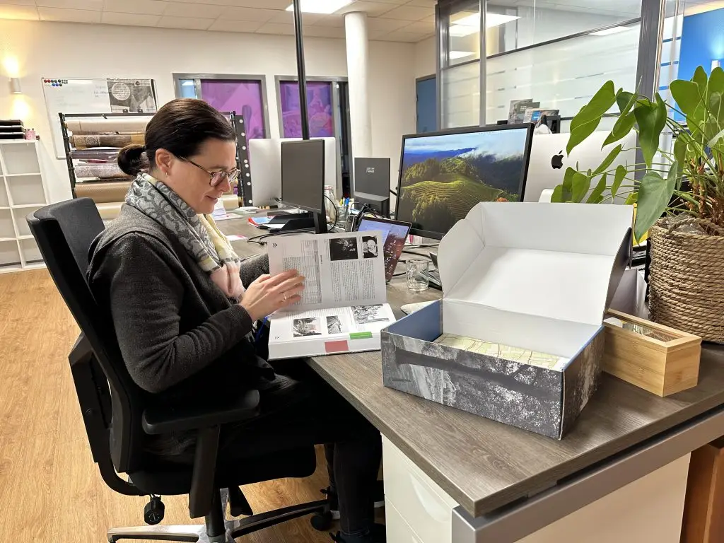 Vormgeefster Martine bladert in het vuistdikke boek Buiten Verwachting van René Hoebeke. Origin Marketing verzorgde vormgeving en drukwerk.